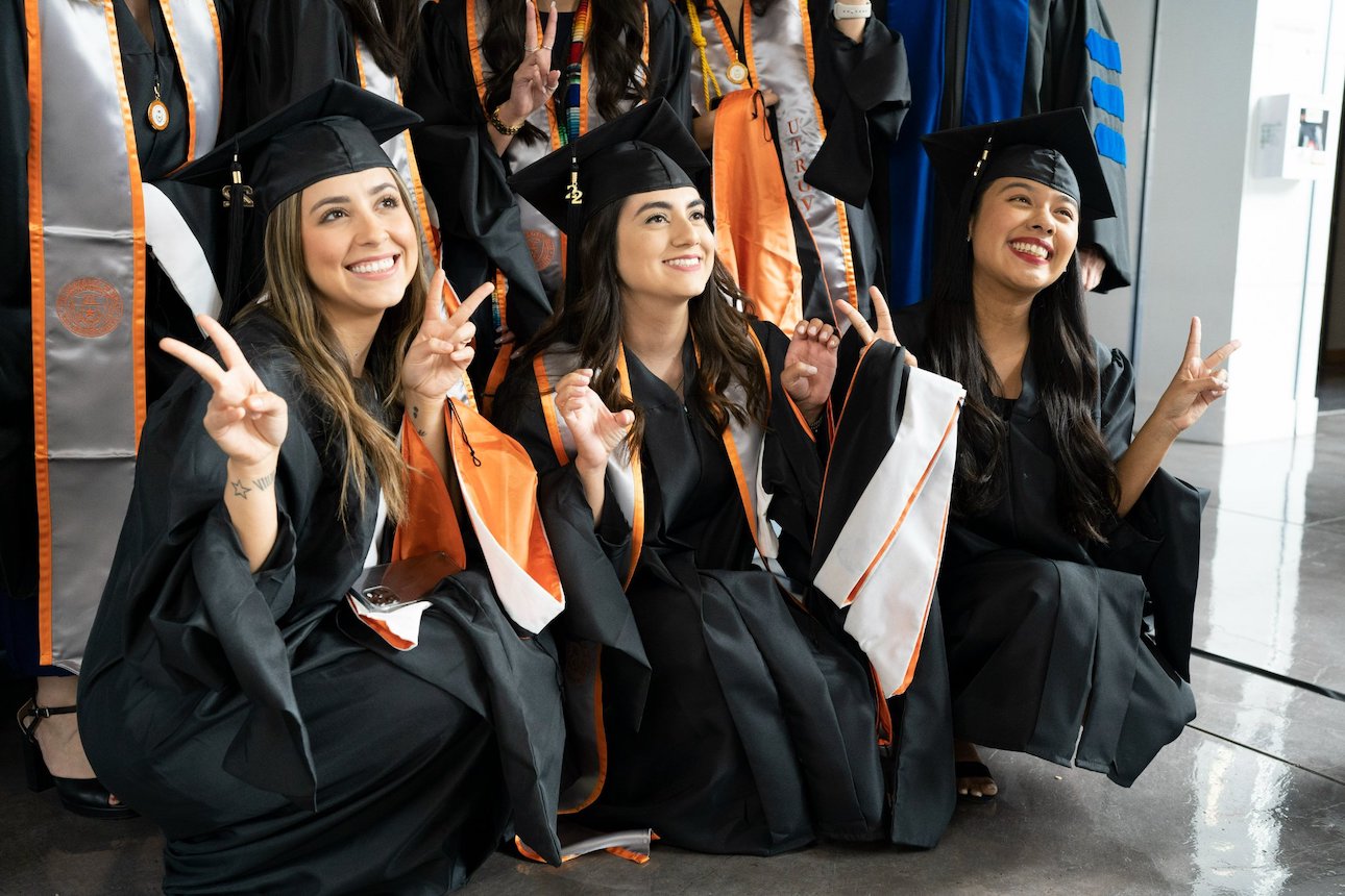 Students in cap and gown with v's up smiling