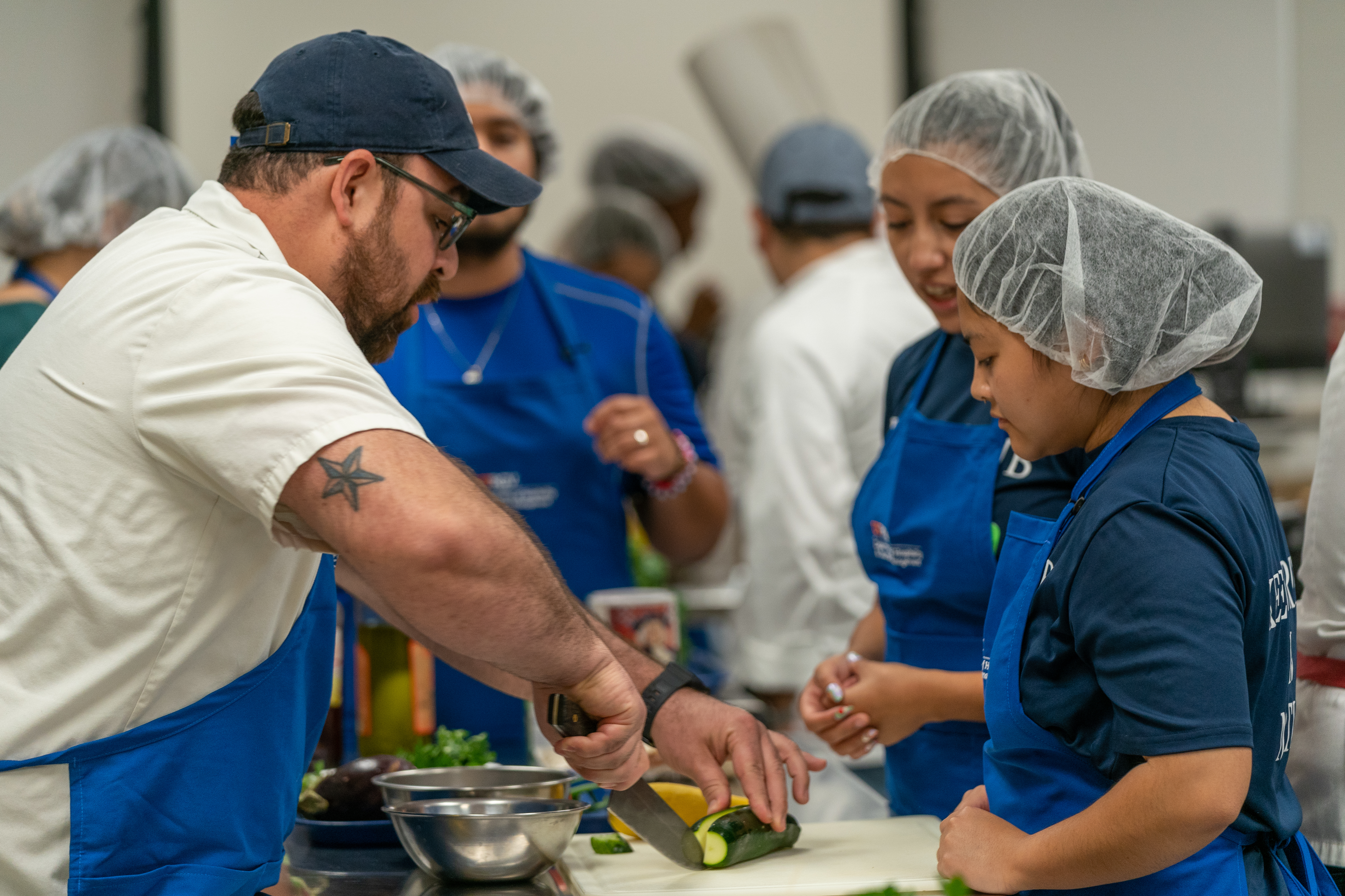 Chet showing two CFSI volunteer show to cut ingredients properly for Iron Chef Competition Page Banner 