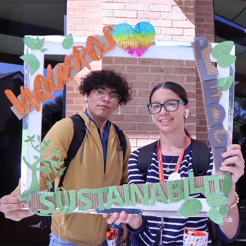 Two students on the Edinburg Campus taking a photo with the Sustainability Pledge selfie frame during Campus Sustainability Day hosted by the Office for Sustainability