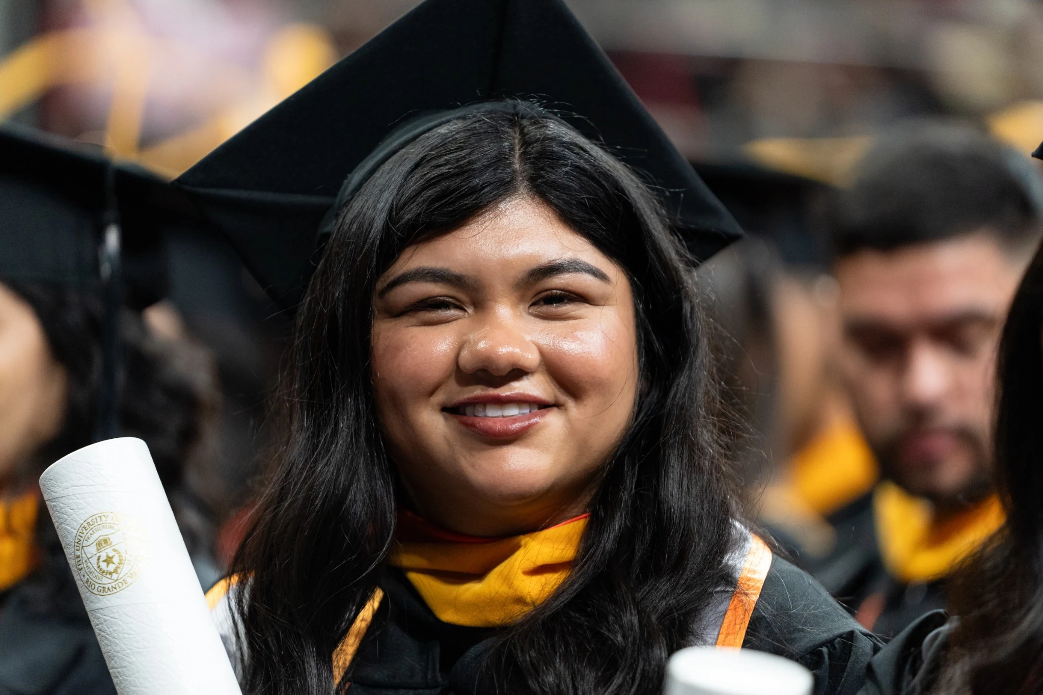UTRGV graduate smiling and holding her diploma during spring commencement.