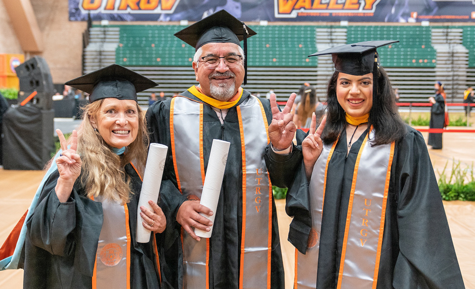 Family of UTRGV graduate college graduates smile at camera in cap and gown holding their diplomas
