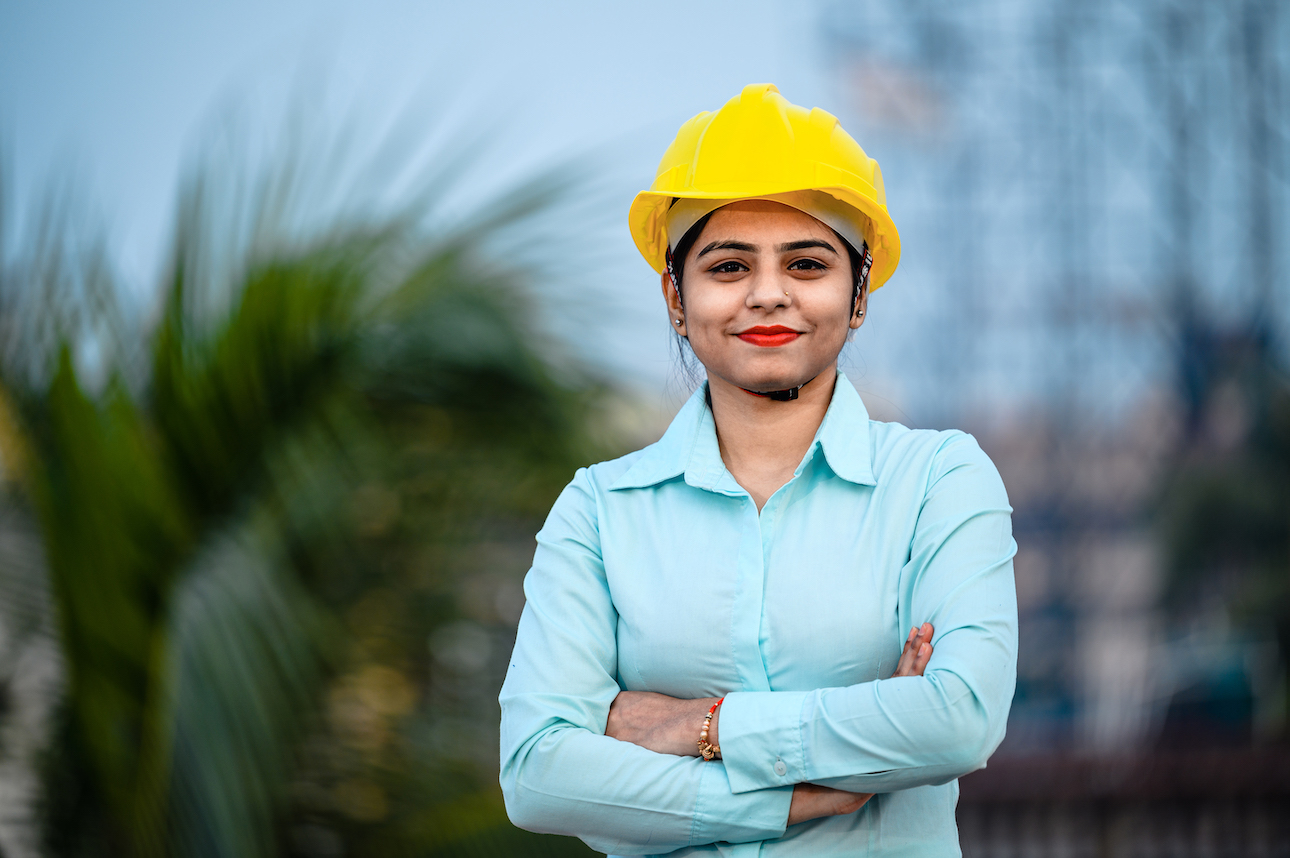 image of student in yellow work helmet smiling at camera with arms crossed