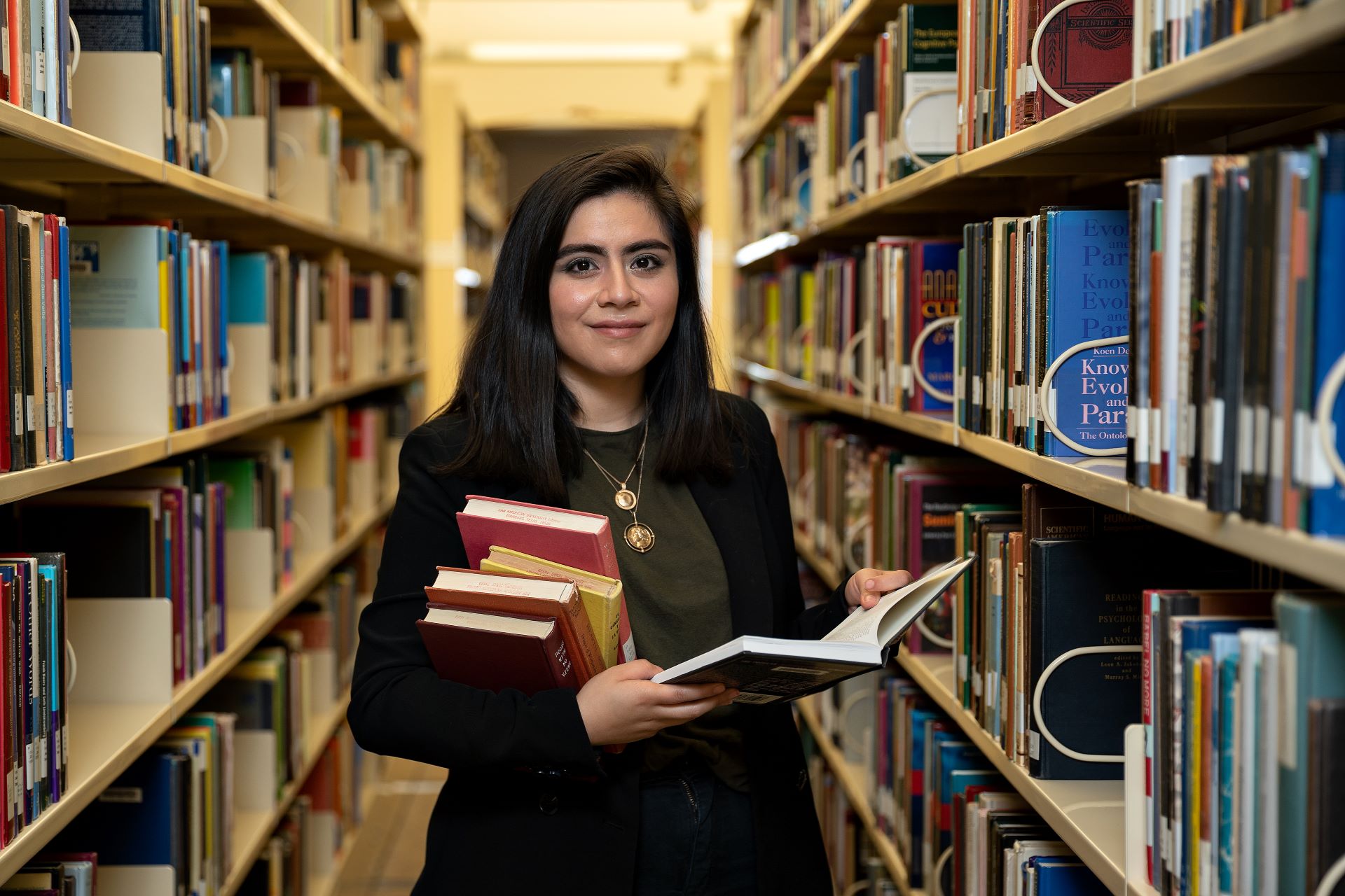 Female student in library aisle with book in hand