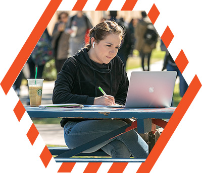 student taking notes while studying on a picnic table with laptop open