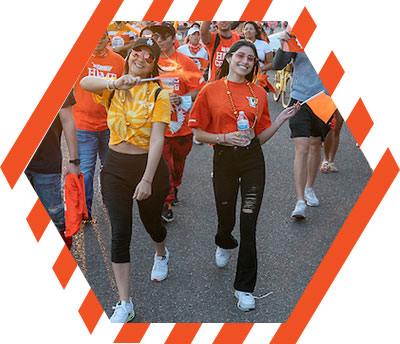 Two female student walking in the Homecoming parade waving orange flags
