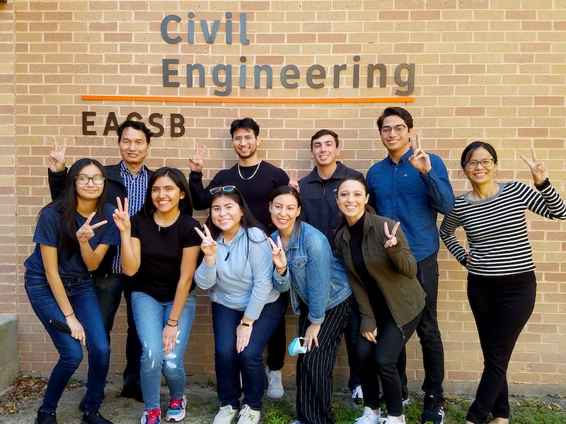 Students standing outside of civil engineering building with v's up smiling