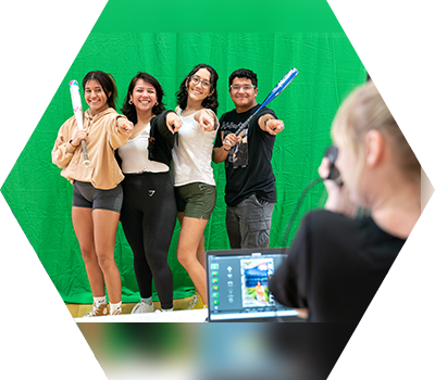 Students stand in front of green screen smiling with photographer taking their picture