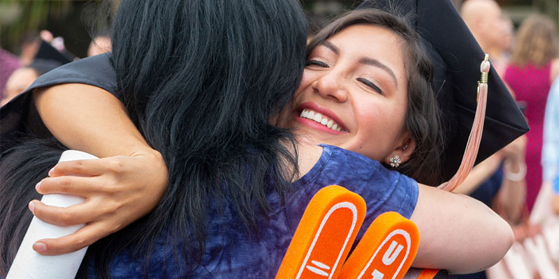 Female graduate holding a diploma and hugging a loved one.