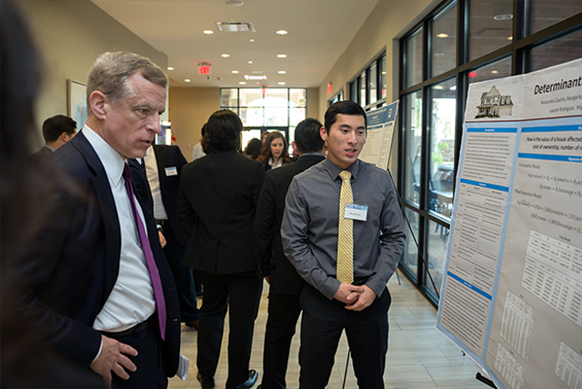 UTRGV student Brandon Lau talks about his group's research project with Robert Kaplan, president and CEO of the Federal Reserve Bank of Dallas, during the Border Economic Development and Entrepreneurship Symposium (BEDES) hosted by UTRGV, the Federal Reserve Bank of Dallas-San Antonio Branch, and the McAllen Chamber of Commerce. The symposium was held Friday, Dec. 1, at the Embassy Suites in McAllen. (UTRGV Photo by Paul Chouy)