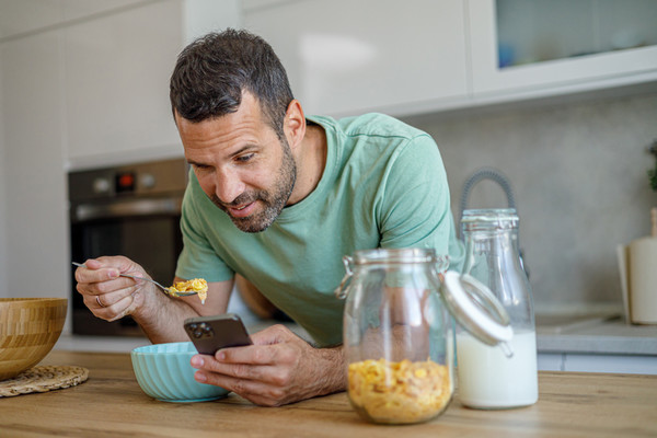 A young man eating while looking at his smartphone