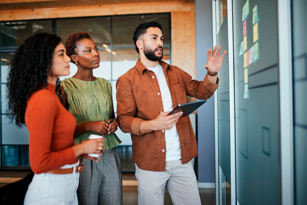 Three professionals reviewing notes on a glass board. 