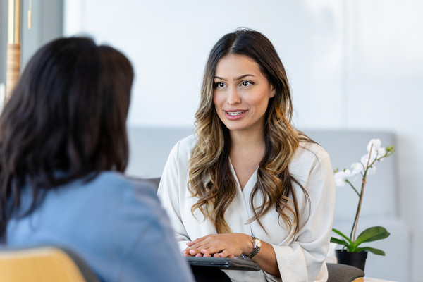 Smiling student holds books on campus walkway surrounded by trees