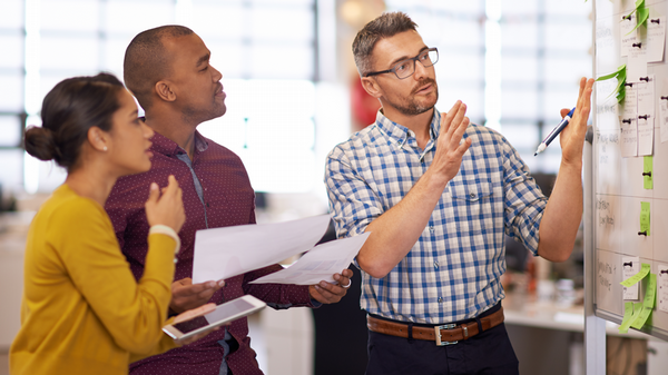 Three professionals review documents and collaborate during a workplace planning session.