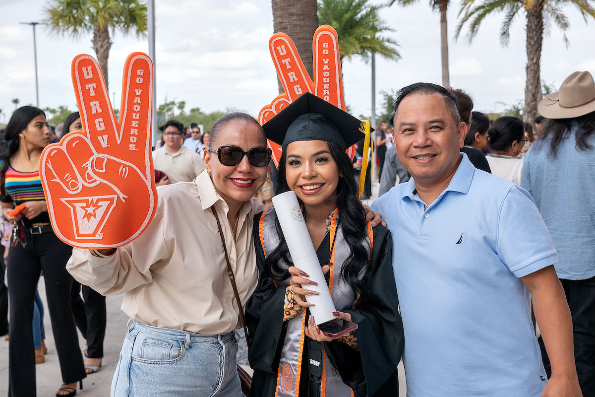 Parents with their graduate, holding V's Up foam hands.