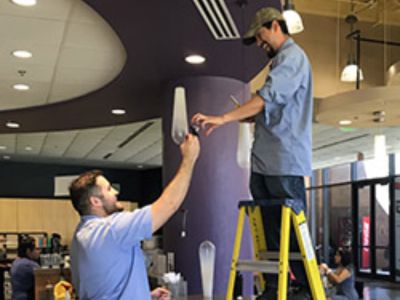 two blue shirt workers fixing a light bulb