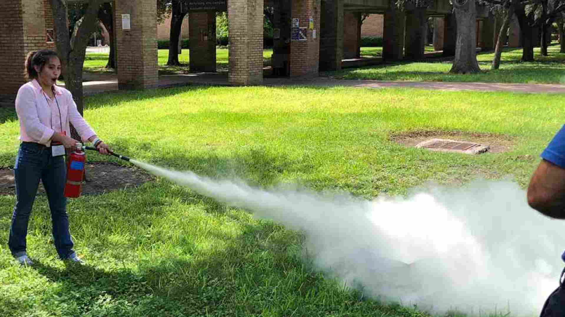 impressed girl in a pink shirt using fire extinguisher for training