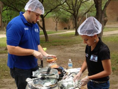 two people preparing hotdog's with food safety attire