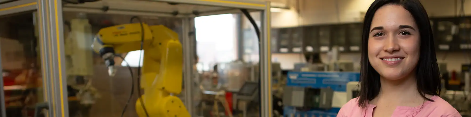 Photo of female student with a robotic arm in the background.