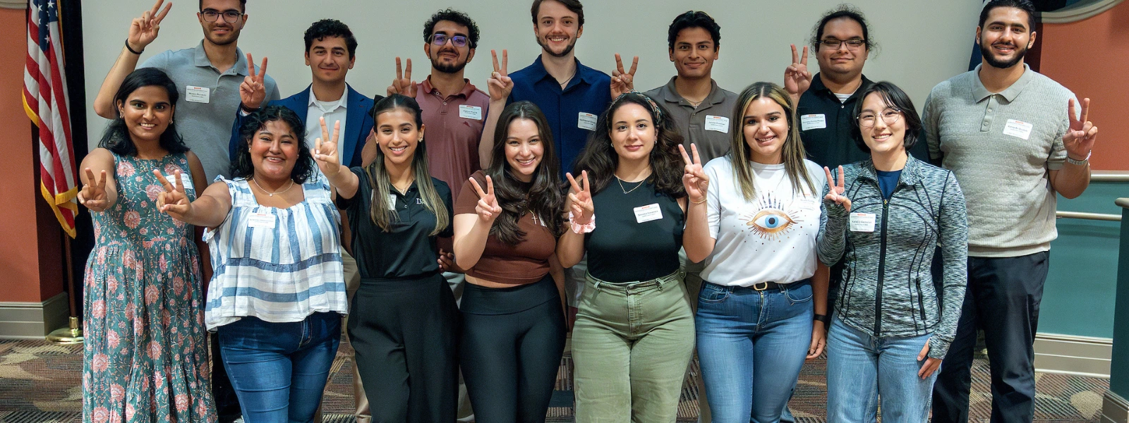 Group of students making “V” signs during a group photo event. 