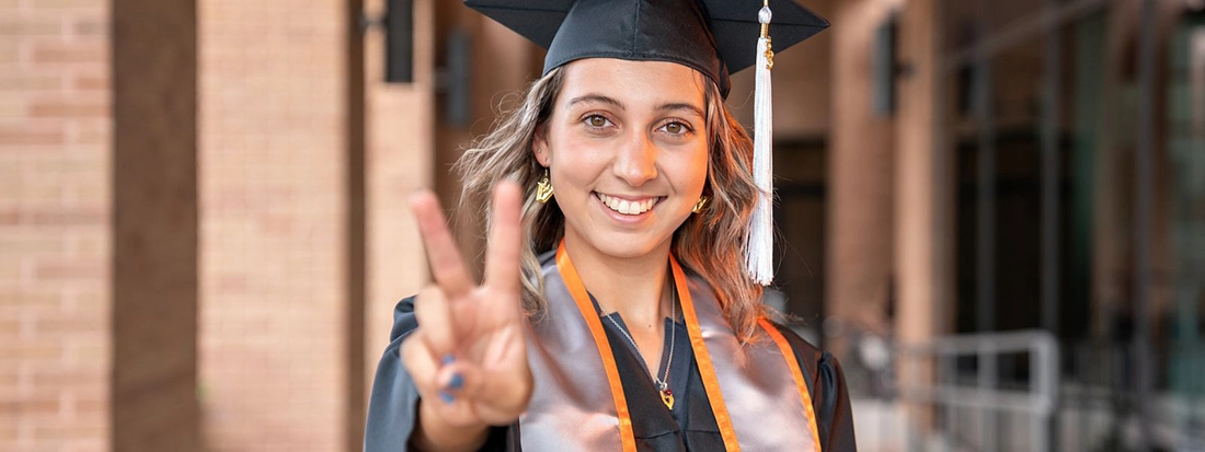 Student in cap and gown signaling v's up. 