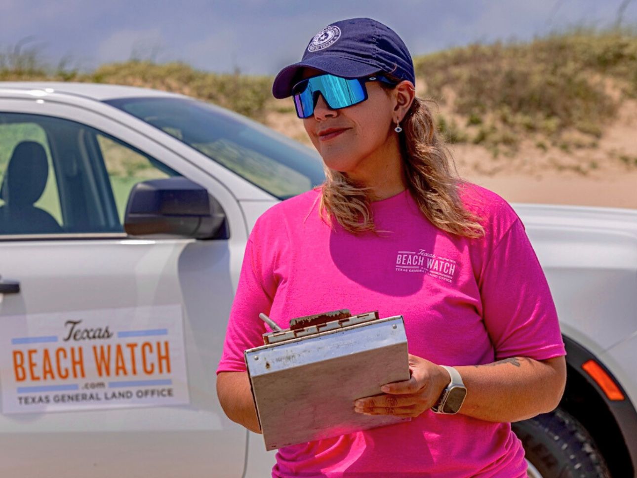 A woman standing next to a pick-up truck on the beach filling out water quality sample forms