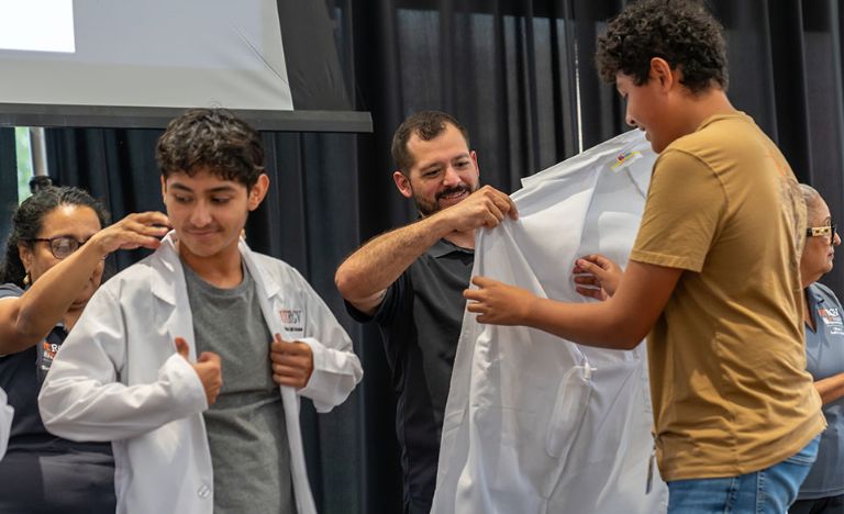 Faculty and handing students white coats during ceremony.
