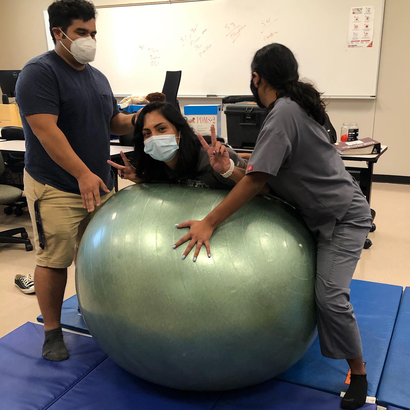 Two students assisting student with balancing their body on a ball.