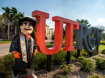 UTRGV mascot graduate poses beside university signage