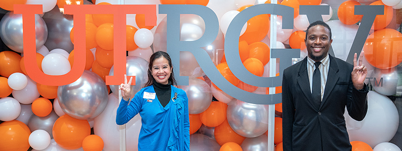 Two staff members with orange, silver, and white balloons and UTRGV sign in the background.