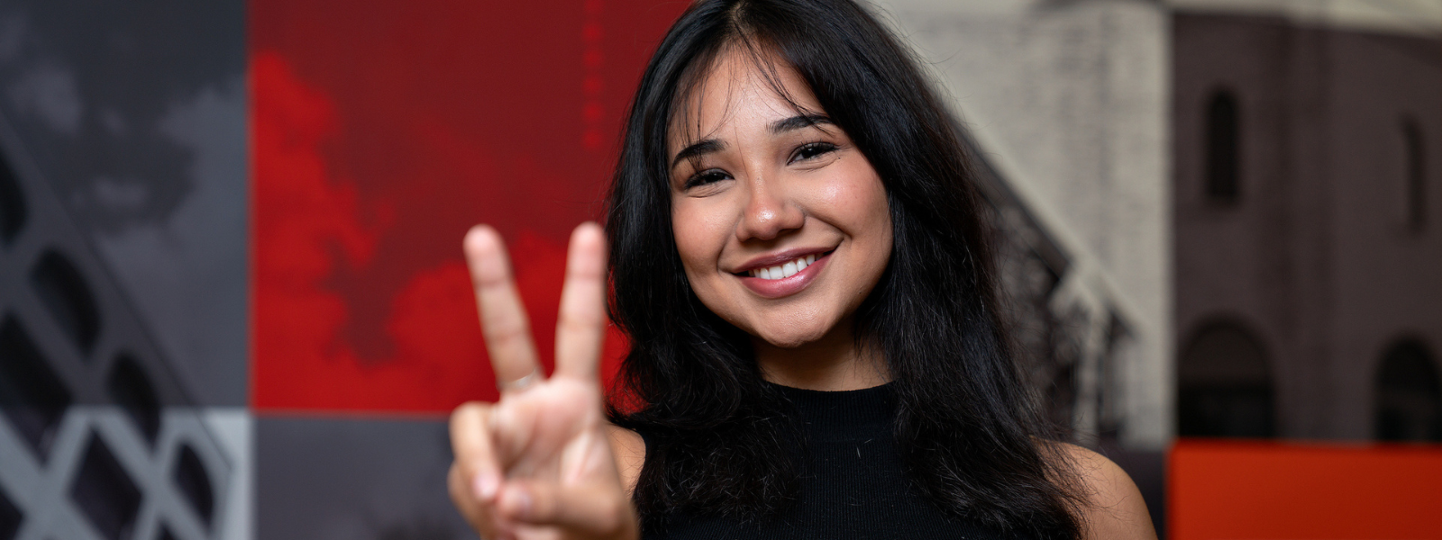 COS student signaling V's up at camera while smiling.