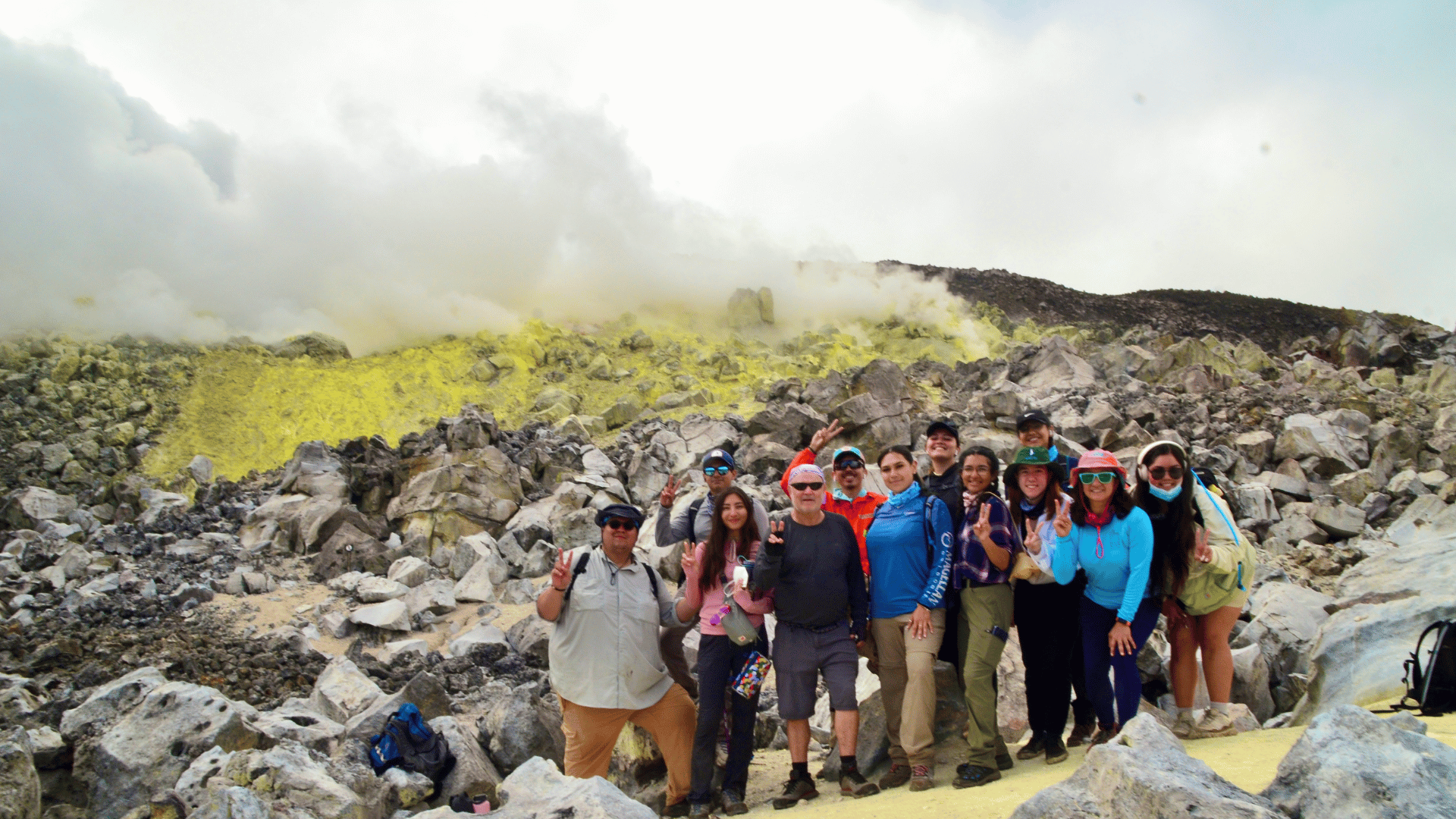 Students posing in front of volcanic rock and yellow fumes