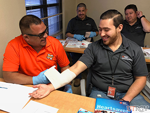 Shuttle Services supervisor practices first aid for an open wound on his coworker.