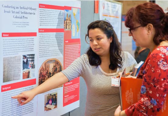 Student presenter pointing and explaining her research presentation at the Engaged Scholar Symposium
