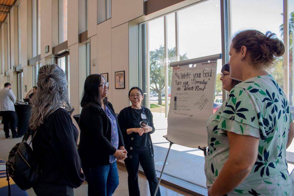 Faculty attending the 14 day writing challenge and talking next to an easel where they wrote their writing goals