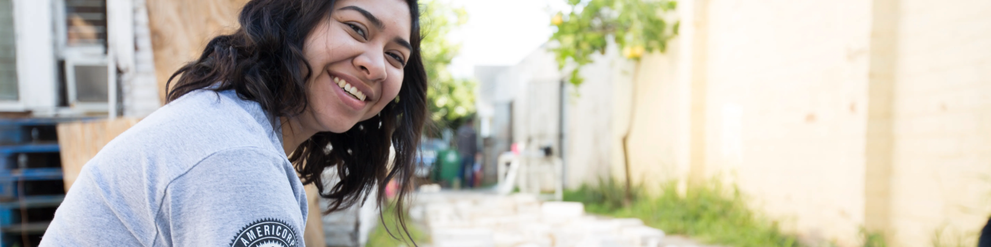 An AmeriCorps member smiling at the camera while working outside on a project.