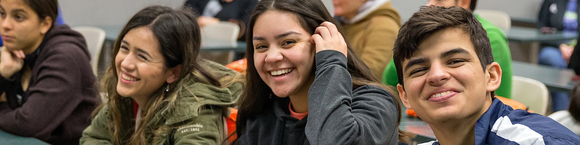 Three students sitting at a classroom table and smiling.