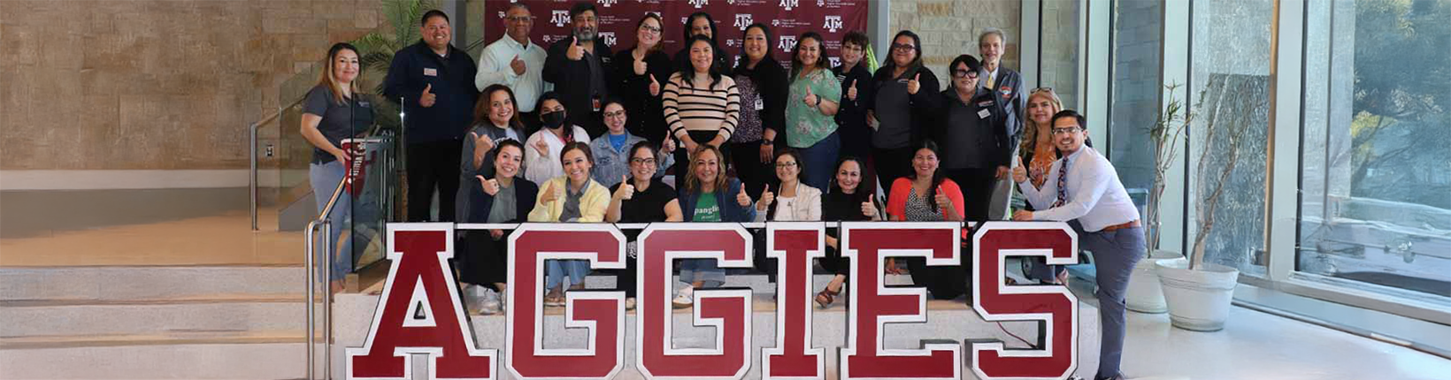 gear-up-staff-and-coordinators-posing-behind-texas-aggies-sign-thumbs-up
