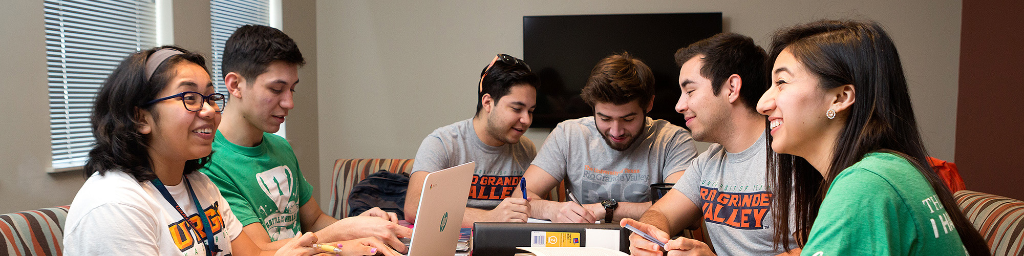 Group of students sitting around a table in a study area, collaborating with laptops, notebooks, and papers spread out.