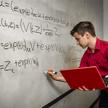 erson writing complex mathematical equations on a large whiteboard while holding a red laptop.