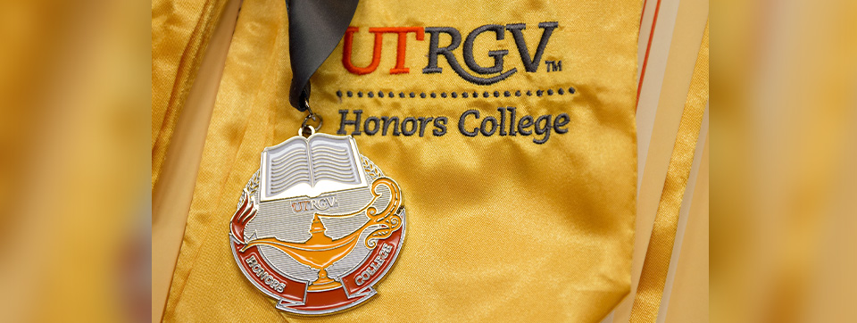 Medal with the words Honors College laying on top of a gold shirt with the Honors College logo.