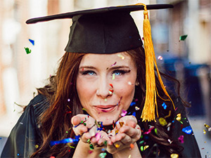 Student with cap and gown blows confetti to the frame