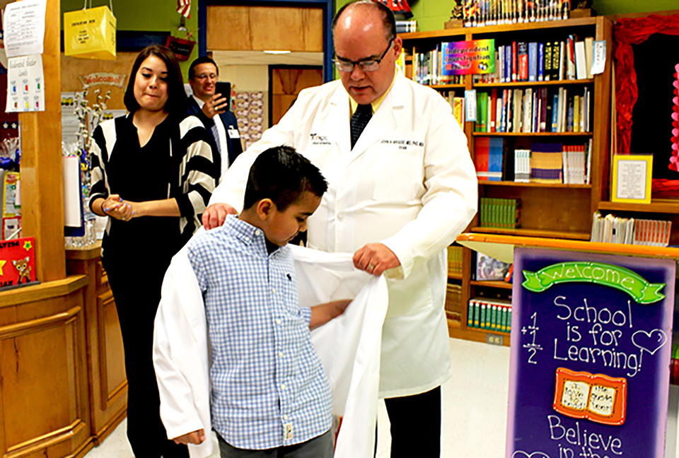 Dr. John Krouse, dean of the UTRGV School of Medicine and executive vice president for Health Affairs at UTRGV, presents Justin Maya, a fourth-grade student at Escandon Elementary School in McAllen, with his very first white coat. (UTRGV Photo)