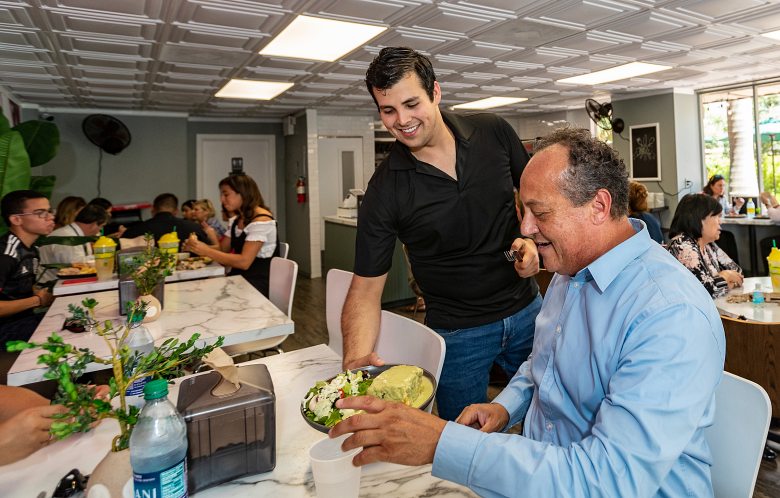 Hector Zavala hans a food dish to sitting customer