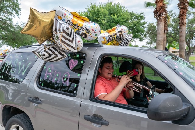 A social work graduate's family member celebrates by playing the trumpet during the UTRGV School of Social Work drive-through hooding ceremony