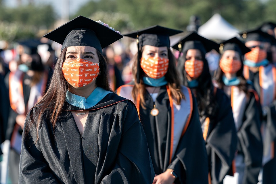 Class of 2021 graduates wearing thier cap & gowns and face coveringss, 