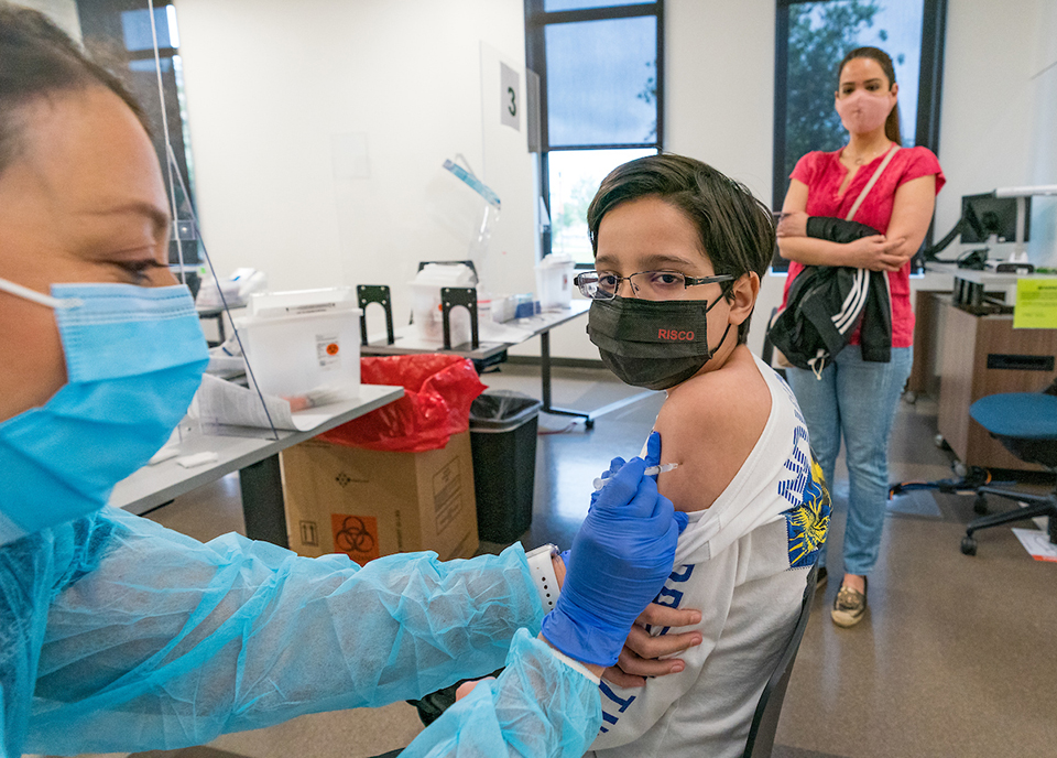 Fernando Perez gets his first vaccine shot while his mother, Nereyda, watches at a distance. (UTRGV Photo by David Pike)