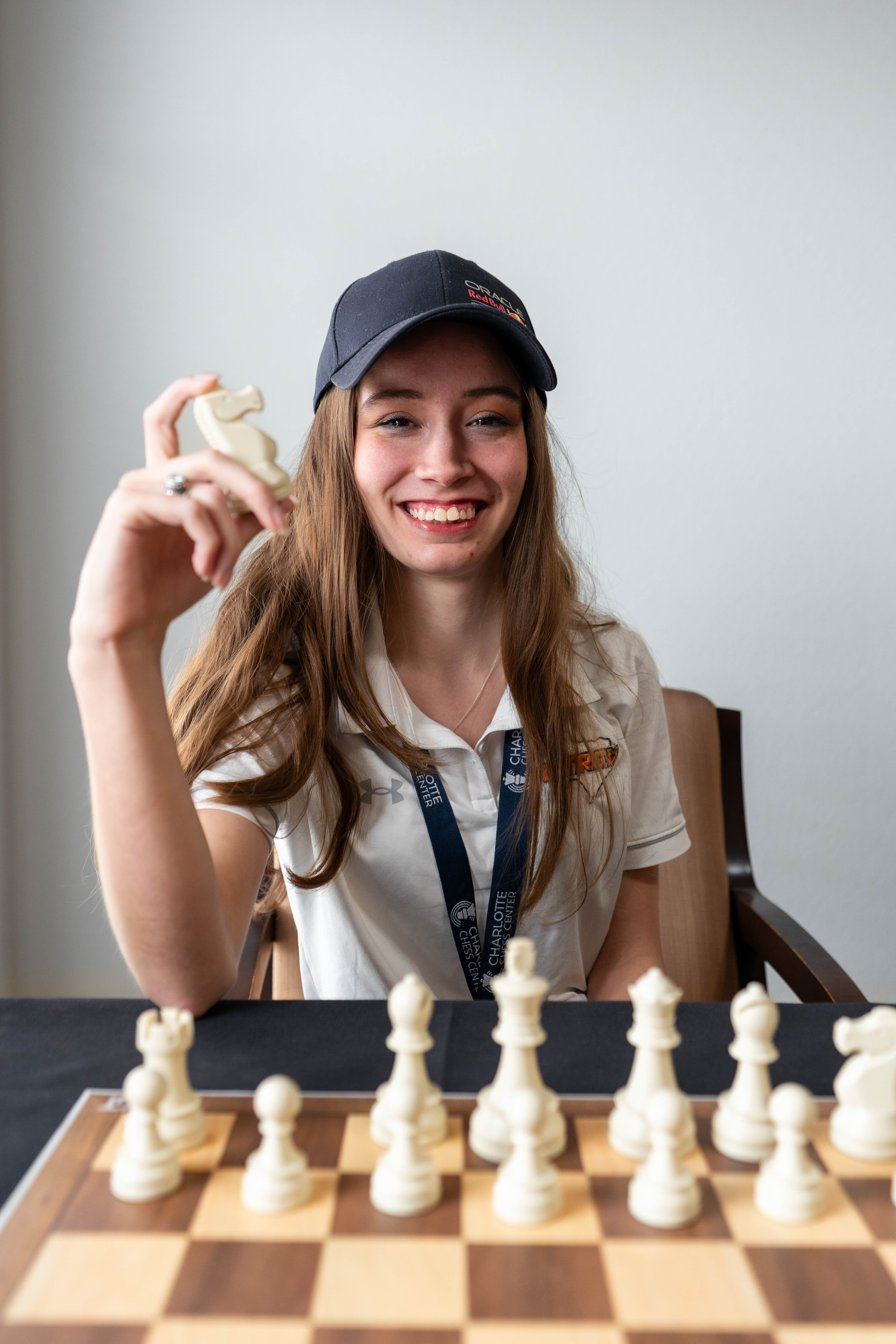 Woman holding up a chess piece wearing a white polo shirt