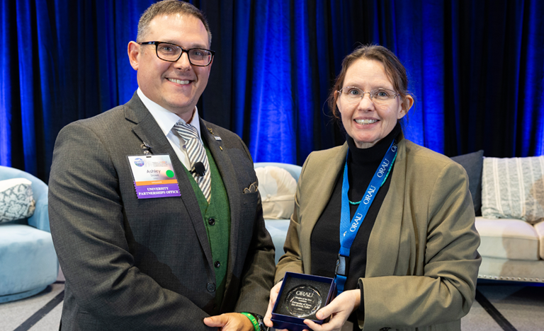 Two attendees standing indoors on a stage, with one ...