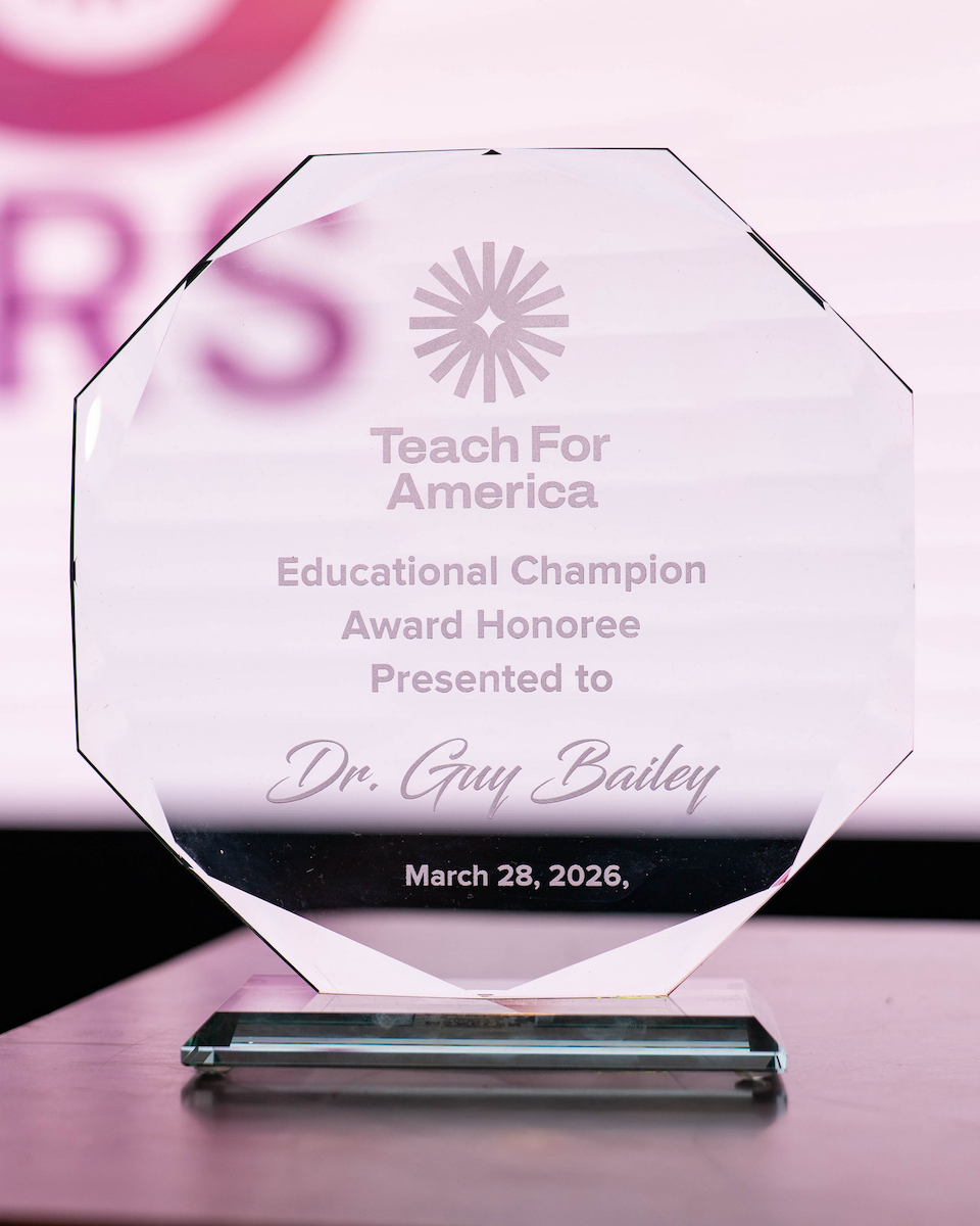 Close-up of a glass award plaque engraved with the Teach For America logo and text recognizing an Educational Champion Award honoree