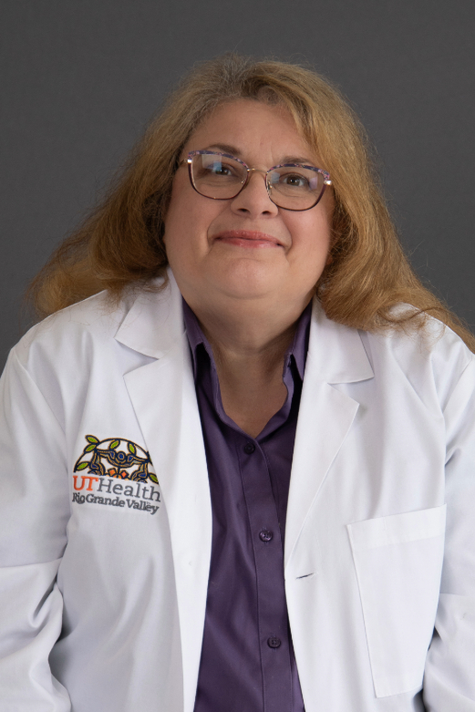 A woman with long blonde hair wearing glasses and a white coat embroidered with "UT Health Rio Grande Valley" over a purple shirt, smiles softly.